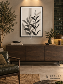 Botanical Shadow by FREMAT: botanical leaves and shadows in a black PVC frame with a printed white border, displayed in a styled interior.