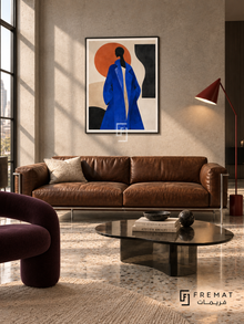 Fashion Block cobalt-blue coat portrait in a slim black PVC frame with a white printed border, displayed above a tobacco sofa in a modern loft.