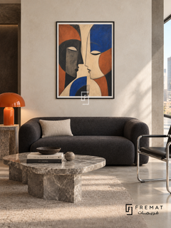 Two Faces by FREMAT in a matte black PVC frame with a flat white printed border. Graphic penthouse lounge: bone-white polished plaster wall, 160cm charcoal wool loveseat, black tubular chrome cantilever chair right, irregular grey marble coffee table, pale concrete floor, soft overhead daylight and vivid orange ceramic lamp.