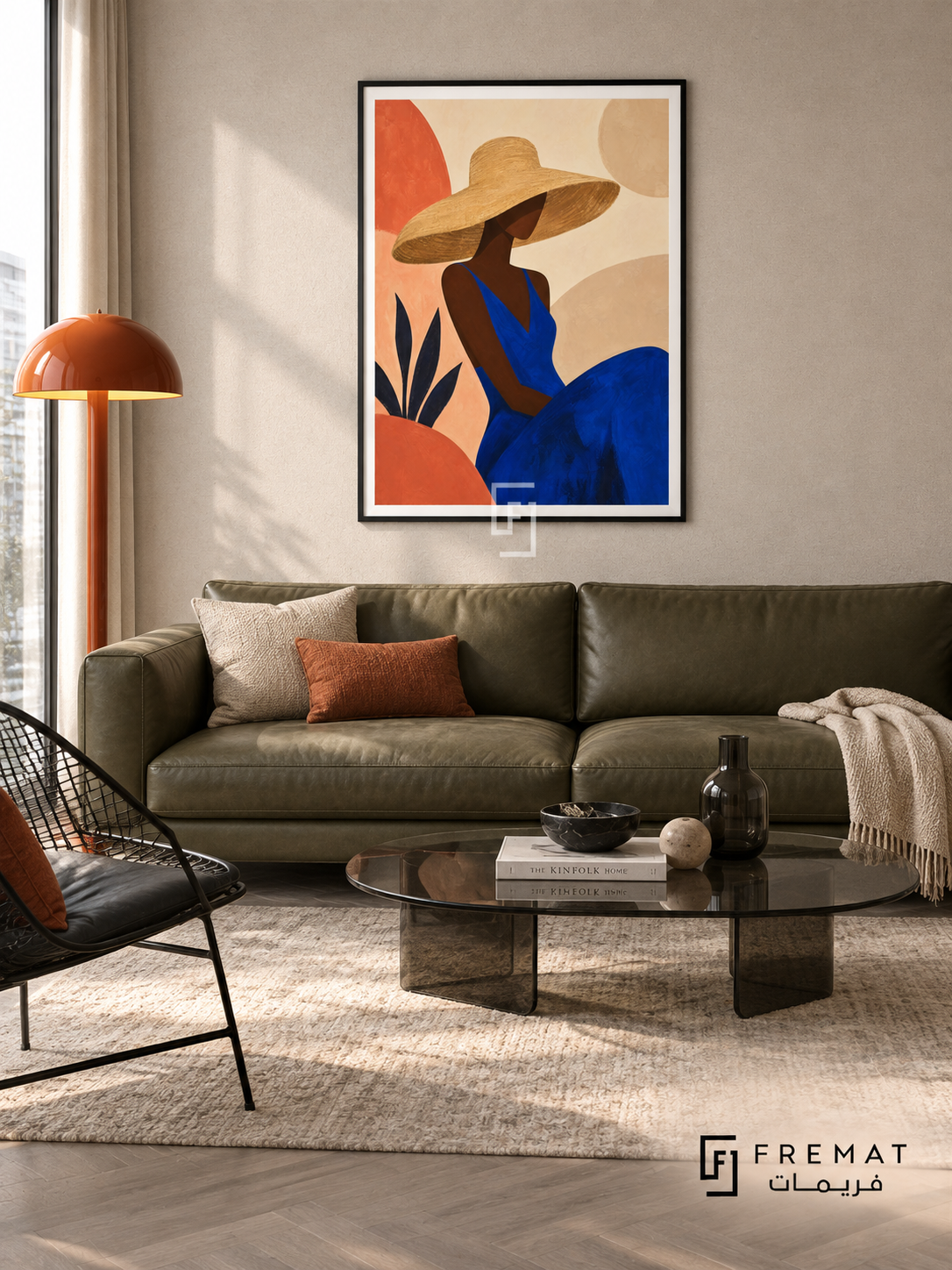 Sun Hat by FREMAT in a matte black PVC frame with a flat white printed border. Fashion apartment lounge: pale oatmeal fabric wall, 160cm olive leather sofa below artwork, black wire accent chair at left, low oval smoked-glass table, grey parquet, cool even daylight and sculptural orange floor lamp.