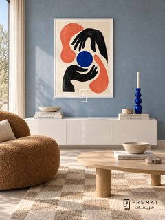 Graphic Hands by FREMAT in a satin white PVC frame with a flat white printed border. Soft graphic living area: faded blue plaster wall, 150cm white lacquer lowboard, warm camel boucle chair left, oval pale wood coffee table, cream checker rug, bright indirect daylight and cobalt sculptural candlestick.
