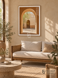 Courtyard Window (PLC03) framed architectural wall art with a light wood-grain PVC frame, flat white paper border and glass reflection. Earthy Mediterranean living room, limewashed sand wall, woven rush sofa 170cm with oatmeal cushions.