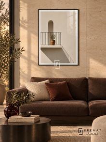 Sunlit Balcony (PLC07) framed architectural wall art with a matte black PVC frame, flat white paper border and glass reflection. Warm minimalist lounge, creamy travertine tile wall, dark brown sofa 175cm.