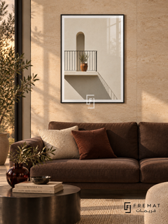 Sunlit Balcony (PLC07) framed architectural wall art with a matte black PVC frame, flat white paper border and glass reflection. Warm minimalist lounge, creamy travertine tile wall, dark brown sofa 175cm.