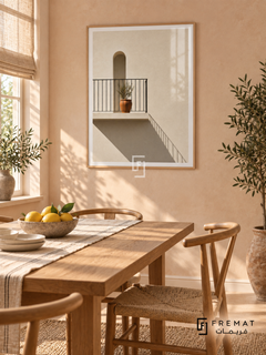 Sunlit Balcony (PLC07) framed architectural wall art with a light wood-grain PVC frame, flat white paper border and glass reflection. Breezy breakfast room, soft peach plaster, oak dining table 150cm.