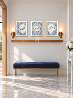 FREMAT Porcelain Devotion shelf set with three 30 x 40 cm gold frames, 2 cm white borders, honey wood shelf and two warm sensor lamps. Morning refined hallway, white wall with narrow moulding, navy blue bench on brass legs, pale grey marble floor, light oak doorway left, white hydrangeas right.