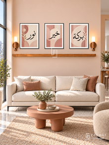 FREMAT Blush Geometry shelf set with three 30 x 40 cm black frames, 2 cm white borders, honey wood shelf and two warm sensor lamps. Morning geometric contemporary lounge, pale peach wall, black-legged ivory sofa, terracotta sculptural coffee table, pale terrazzo floor, window left.