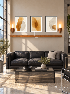 FREMAT Amber Glass shelf set with three 30 x 40 cm black frames, 2 cm white borders, honey wood shelf and two warm sensor lamps. Morning industrial loft lounge, pale amber plaster wall, black tubular leather sofa, rectangular smoked glass coffee table, pale concrete, steel gridded sunny window left.