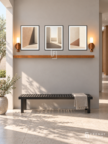 FREMAT Shadow Courtyard shelf set with three 30 x 40 cm black frames, 2 cm white borders, honey wood shelf and two warm sensor lamps. Morning architectural corridor, soft warm grey wall, black slatted bench, large pale stone tiles, sunny courtyard opening left casting geometric shadows, restrained contemporary decor.