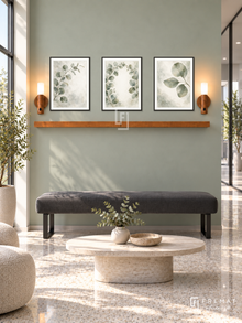 FREMAT Eucalyptus Mist shelf set with three 30 x 40 cm black frames, 2 cm white borders, honey wood shelf and two warm sensor lamps. Morning modern wellness waiting room, pale eucalyptus green plaster wall, charcoal upholstered bench and pale oval stone table, cream terrazzo floor, wide sunny window left, glass corridor right.