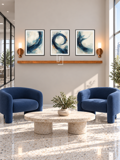 FREMAT Forward Current shelf set with three 30 x 40 cm black frames, 2 cm white borders, honey wood shelf and two warm sensor lamps. Morning contemporary shared office entry, pale taupe display wall, cobalt tubular lounge chairs, low oval travertine table, cream terrazzo floor, wide bright window at right and glazed corridor left.