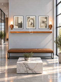 FREMAT Balanced Structure shelf set with three 30 x 40 cm black frames, 2 cm white borders, honey wood shelf and two warm sensor lamps. Morning modern engineering office reception, pale mineral grey display wall, black steel and tan leather bench, low cube marble table, polished concrete floor, generous factory glazing right, open corridor left.
