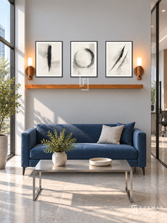 FREMAT Quiet Focus shelf set with three 30 x 40 cm black frames, 2 cm white borders, honey wood shelf and two warm sensor lamps. Morning minimalist finance office entry, pearl grey display wall, cobalt compact sofa, rectangular brushed steel table, large pale stone floor tiles, tall sunlit window left and glass office door right.