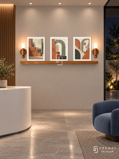 FREMAT Terrace Rhythm shelf set with three 30 x 40 cm white frames, 2 cm white borders, honey wood shelf and two warm sensor lamps. Night contemporary office reception, pale clay display wall, white rounded desk at lower left and blue lounge chair right, stone tiled floor, dark courtyard right, soft ceiling downlights.