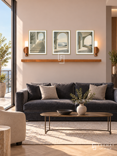 FREMAT Open Perspective shelf set with three 30 x 40 cm gold frames, 2 cm white borders, honey wood shelf and two warm sensor lamps. Morning contemporary executive lounge, pale blush beige display wall, charcoal velvet sofa, narrow bronze table, light herringbone floor, sunny balcony glazing left.