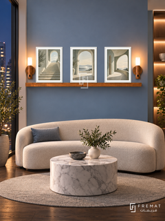 FREMAT Open Perspective shelf set with three 30 x 40 cm white frames, 2 cm white borders, honey wood shelf and two warm sensor lamps. Night modern business waiting lounge, dusty blue display wall, cream curved bench, white marble drum table, dark oak floor, city window left and illuminated niche right.