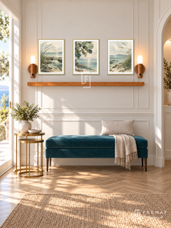FREMAT Tidal Botanicals shelf set with three 30 x 40 cm gold frames, 2 cm white borders, honey wood shelf and two warm sensor lamps. Morning elegant coastal corridor, ivory panelled wall, teal velvet bench, brass nesting tables, herringbone oak, broad sunlit doorway left and narrow arched niche right.