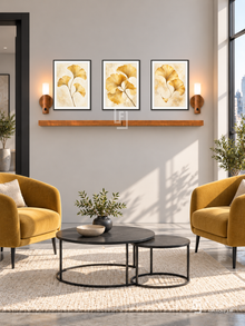 FREMAT Ginkgo Gold shelf set with three 30 x 40 cm black frames, 2 cm white borders, honey wood shelf and two warm sensor lamps. Morning urban contemporary lounge, pale warm grey wall, mustard accent armchairs, black metal nesting tables, concrete floor with cream rug, broad window right, black doorway left.