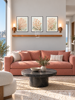 FREMAT Coral Garden shelf set with three 30 x 40 cm black frames, 2 cm white borders, honey wood shelf and two warm sensor lamps. Morning coastal urban living room, light warm grey wall, coral pink sofa, black stone round table, terrazzo, sea window left and open hallway right.