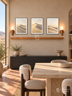 FREMAT Dune Silence shelf set with three 30 x 40 cm black frames, 2 cm white borders, honey wood shelf and two warm sensor lamps. Morning desert modern dining room, sand plaster wall, low black oak sideboard below shelf, travertine dining table edge foreground, terracotta floor, huge dune-facing window left.