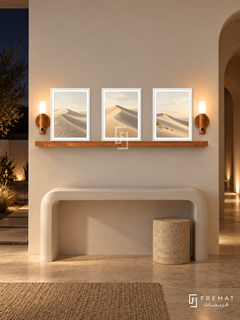 FREMAT Dune Silence shelf set with three 30 x 40 cm white frames, 2 cm white borders, honey wood shelf and two warm sensor lamps. Night minimal desert hallway, ivory wall, curved white console and stone stool, beige limestone floor, deep arched passage right, dark desert courtyard left with warm path lights.