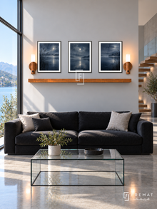 FREMAT Moonlit Lake shelf set with three 30 x 40 cm black frames, 2 cm white borders, honey wood shelf and two warm sensor lamps. Morning lakeside modern lounge, silver-grey wall, black low sofa, glass cube table, polished concrete floor, blue lake view left and floating staircase right.