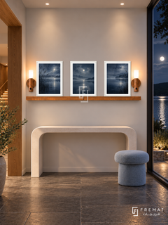 FREMAT Moonlit Lake shelf set with three 30 x 40 cm white frames, 2 cm white borders, honey wood shelf and two warm sensor lamps. Night lake-house entry, pearl wall, white curved console and pale blue stool, slate floor, moonlit lake through large window right, recessed warm lights, oak portal left.
