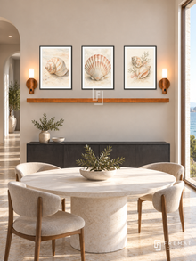 FREMAT Tidal Shells shelf set with three 30 x 40 cm black frames, 2 cm white borders, honey wood shelf and two warm sensor lamps. Morning minimal seaside dining room, pale sand wall, charcoal credenza below shelf, round white dining table foreground, limestone floor, ocean window right, curved hall left.