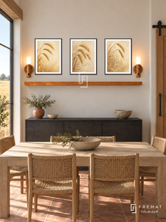 FREMAT Wheat And Wind shelf set with three 30 x 40 cm black frames, 2 cm white borders, honey wood shelf and two warm sensor lamps. Morning modern farmhouse dining space, warm chalk wall, black oak sideboard below shelf, pale timber dining table and woven chairs foreground, terracotta floor, wheat field window left, sliding barn door right.