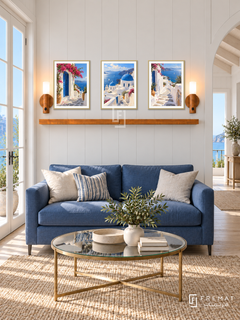 FREMAT Aegean Light shelf set with three 30 x 40 cm gold frames, 2 cm white borders, honey wood shelf and two warm sensor lamps. Morning elegant coastal salon, white panelled wall, cobalt loveseat, champagne brass glass table, pale oak floor, blue sea French doors left, vaulted opening right.