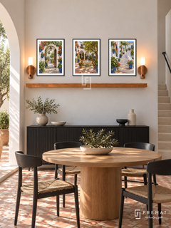 FREMAT Andalusian Patios shelf set with three 30 x 40 cm black frames, 2 cm white borders, honey wood shelf and two warm sensor lamps. Morning Andalusian contemporary dining room, white stucco wall, black sideboard below shelf, round oak table and black chairs, patterned terracotta floor, courtyard arch left, slim stone stair right.