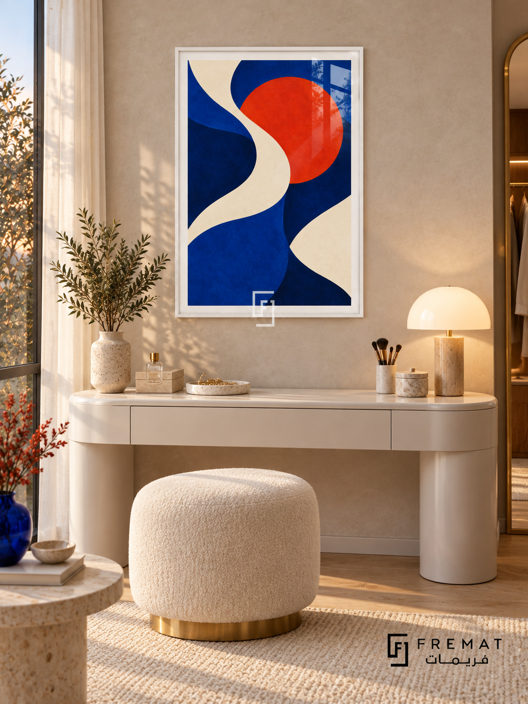 Cobalt Current: An ivory ribbon winds through cobalt and deep navy fields beside a vivid vermilion disc. White PVC frame displayed with a curved white vanity and boucle stool.
