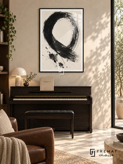 Monochrome Gesture: A sweeping black brushstroke forms an open loop on warm ivory, with dry-brush marks and scattered ink-like splashes. Black PVC frame displayed with a dark upright piano and padded bench.