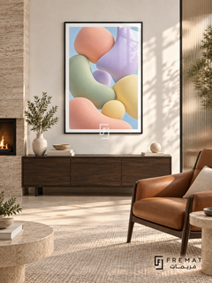Pastel Drift: Softly shaded pebble-like forms in peach, sage, lilac and pale yellow float together against a light blue background. Black PVC frame displayed with a walnut cabinet beside a fireplace and leather chair.