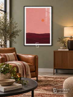 Pink Horizon. A small orange sun floats above a low burgundy horizon beneath a dusty pink sky. Shown in a Black PVC frame in a styled room.