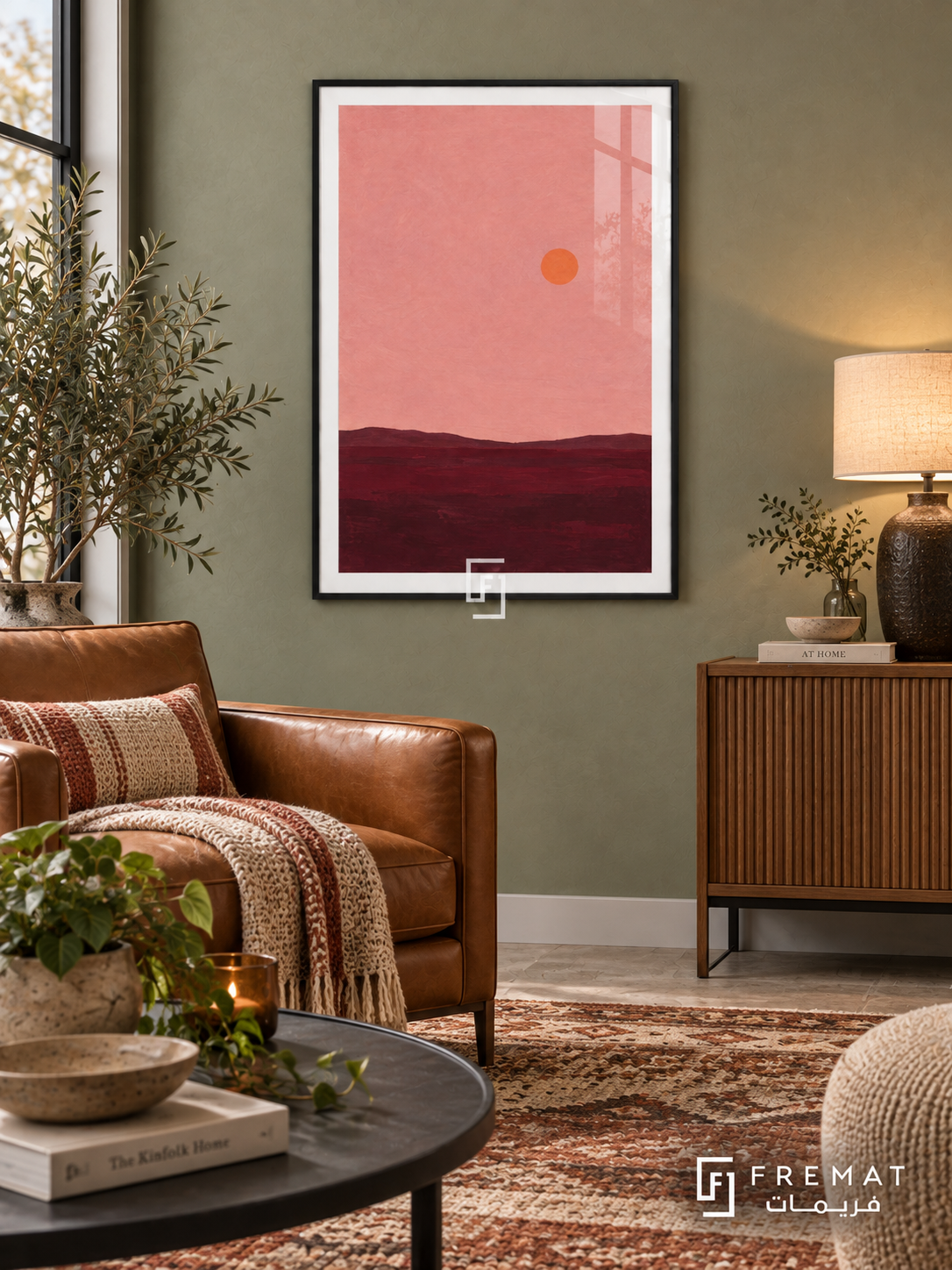 Pink Horizon. A small orange sun floats above a low burgundy horizon beneath a dusty pink sky. Shown in a Black PVC frame in a styled room.