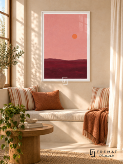 Pink Horizon. A small orange sun floats above a low burgundy horizon beneath a dusty pink sky. Shown in a White PVC frame in a styled room.