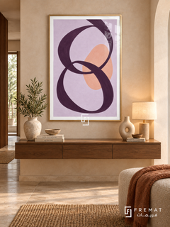 Lilac Loops. A looping plum ribbon crosses a peach oval on a lavender background. Shown in a Gold PVC frame in a styled room.