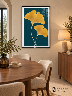 Golden Ginkgo. Two golden-yellow ginkgo leaves with fine veins rise against a deep teal background. Shown in a Black PVC frame in a styled room.