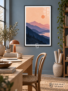 Lavender Mountains. Layered navy and lavender mountains surround pink water beneath a peach sky and orange sun. Shown in a Black PVC frame in a styled room.