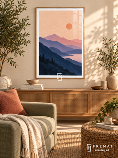 Lavender Mountains. Layered navy and lavender mountains surround pink water beneath a peach sky and orange sun. Shown in a Wooden Texture PVC frame in a styled room.