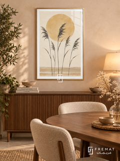 Sun and Reeds. Five delicate dark reed stems stand before an ochre sun above sandy horizontal bands. Shown in a Gold PVC frame in a styled room.