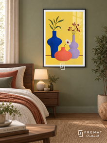 Colorful Still Life. Cobalt, coral and lavender vases hold leaves and flowers against yellow above a burgundy table line. Shown in a Black PVC frame in a styled room.