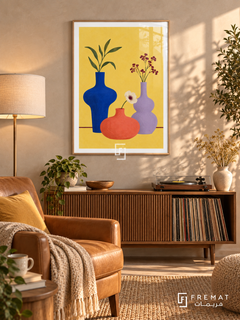 Colorful Still Life. Cobalt, coral and lavender vases hold leaves and flowers against yellow above a burgundy table line. Shown in a Wooden Texture PVC frame in a styled room.