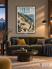 Hill Climb (car09), Black frame with white printed border in a styled interior. A yellow sports car rounds a pale winding mountain road above a blue lake, rocky slopes and evergreen trees. Tall cream lettering reads HILL CLIMB.