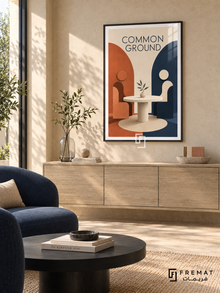 Common Ground (com06), Black frame with white printed border in a styled interior. Two simplified seated figures face each other across a round table with a leafy sprig. Terracotta and navy arches frame the cream scene beneath “COMMON GROUND” in a geometric sculptural illustration.