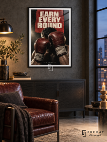 Earn Every Round: Raised oxblood boxing gloves and wrapped wrists emerge from a charcoal and red collage under hard cream light. Black frame with a white printed border, displayed in a styled room.