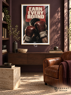 Earn Every Round: Raised oxblood boxing gloves and wrapped wrists emerge from a charcoal and red collage under hard cream light. Gold frame with a white printed border, displayed in a styled room.