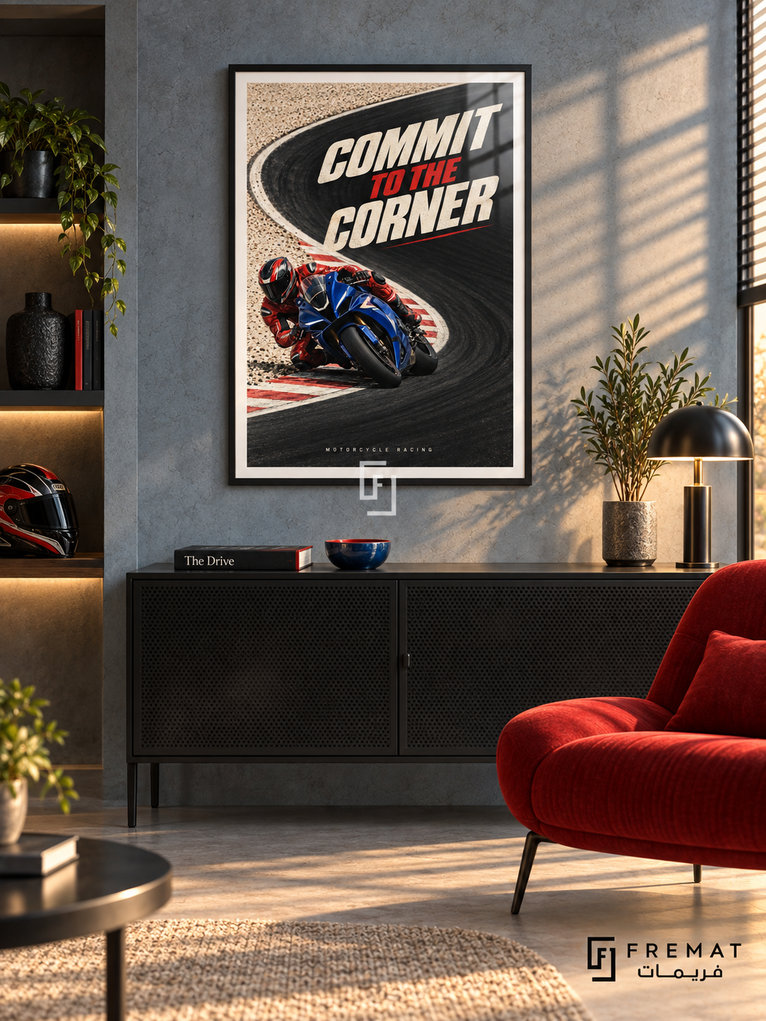 Commit To The Corner: A blue motorcycle and red-suited rider lean into a sweeping black track corner bordered by cream ground and red accents. Black frame with a white printed border, displayed in a styled room.