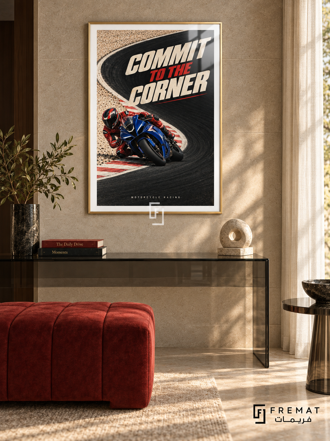 Commit To The Corner: A blue motorcycle and red-suited rider lean into a sweeping black track corner bordered by cream ground and red accents. Gold frame with a white printed border, displayed in a styled room.